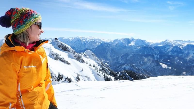 Woman in a colorful cap and yellow jacket looks at snow-covered mountains.