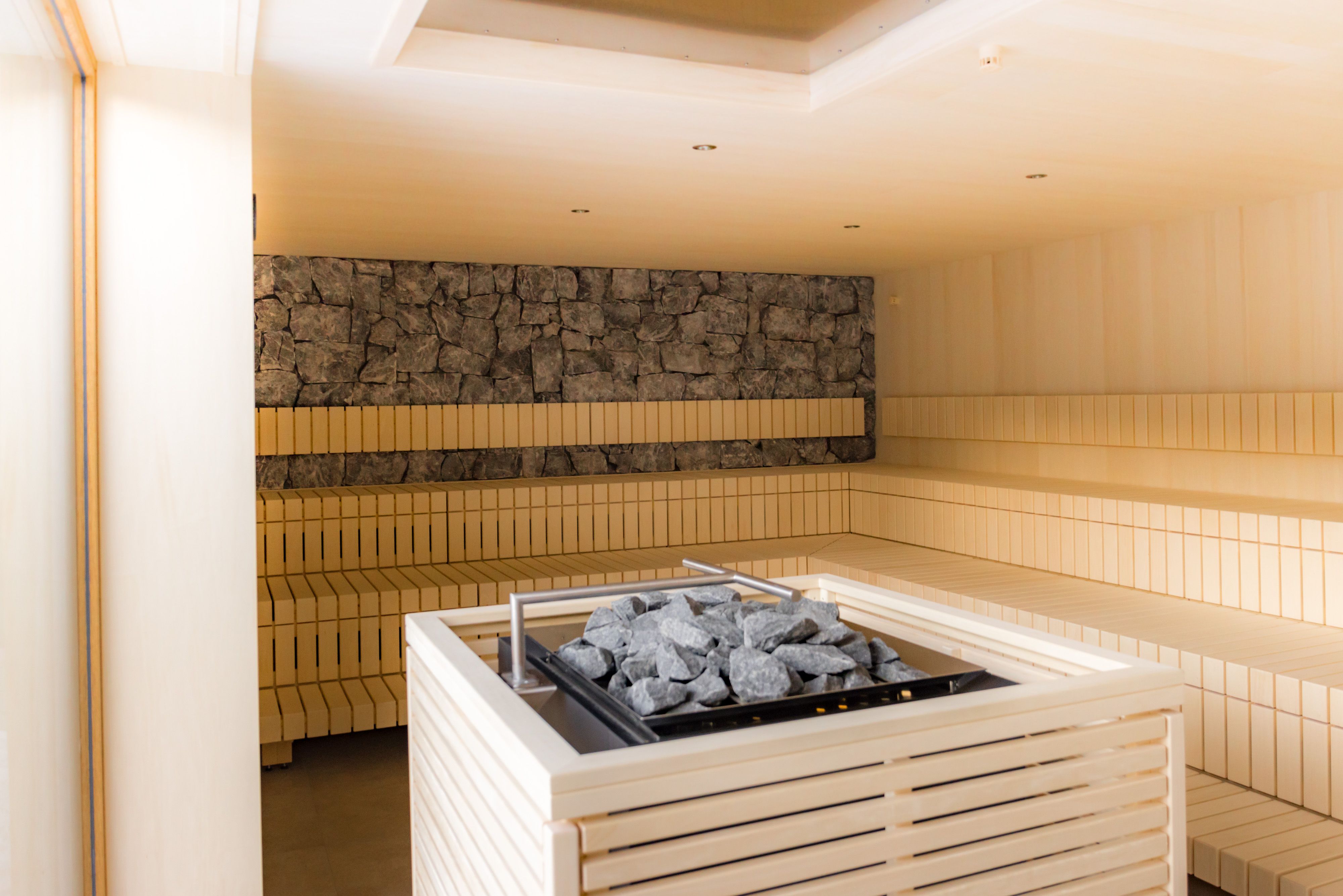 Interior view of a modern sauna with wooden benches and a stove with stones in the middle.