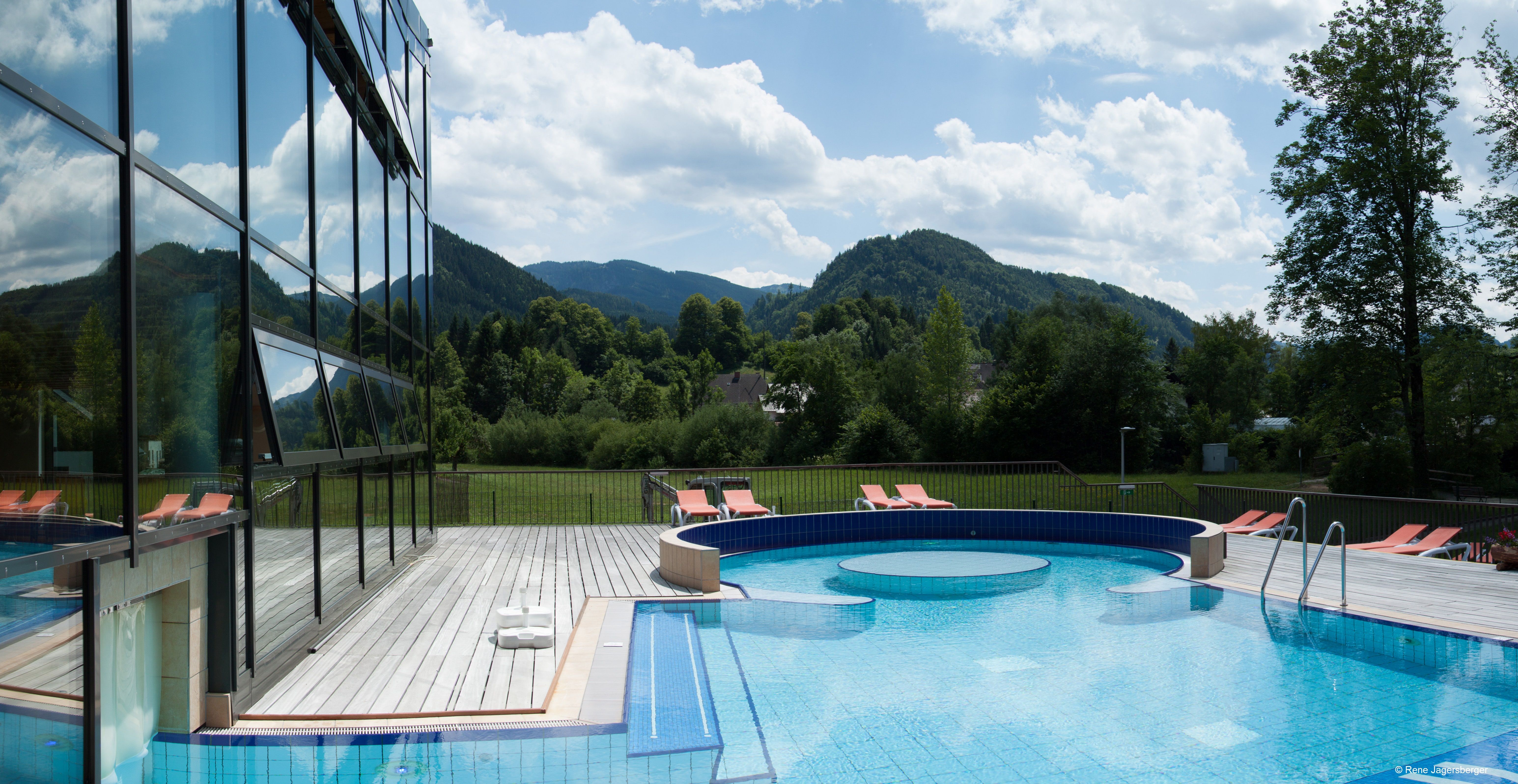 Outdoor area of the Ybbstaler Solebad with pool and sun loungers, surrounded by green hills and trees.