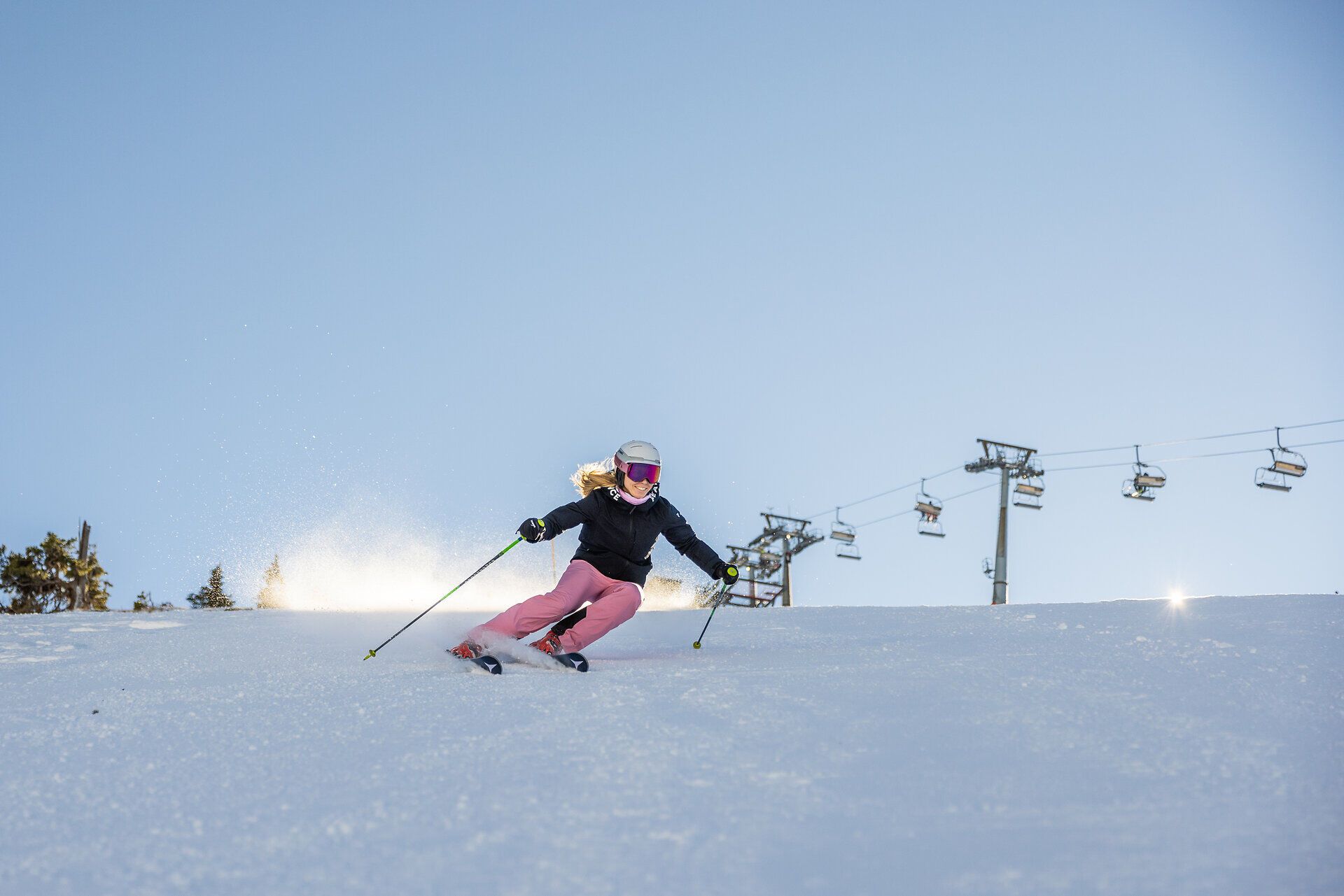 Die strahlende Wintersonne erleuchtet die schneebedeckten Hänge, während eine Skifahrerin elegant die Piste hinuntergleitet. Die frische, kalte Luft und der glitzernde Schnee schaffen eine unvergessliche Atmosphäre für Wintersportliebhaber.