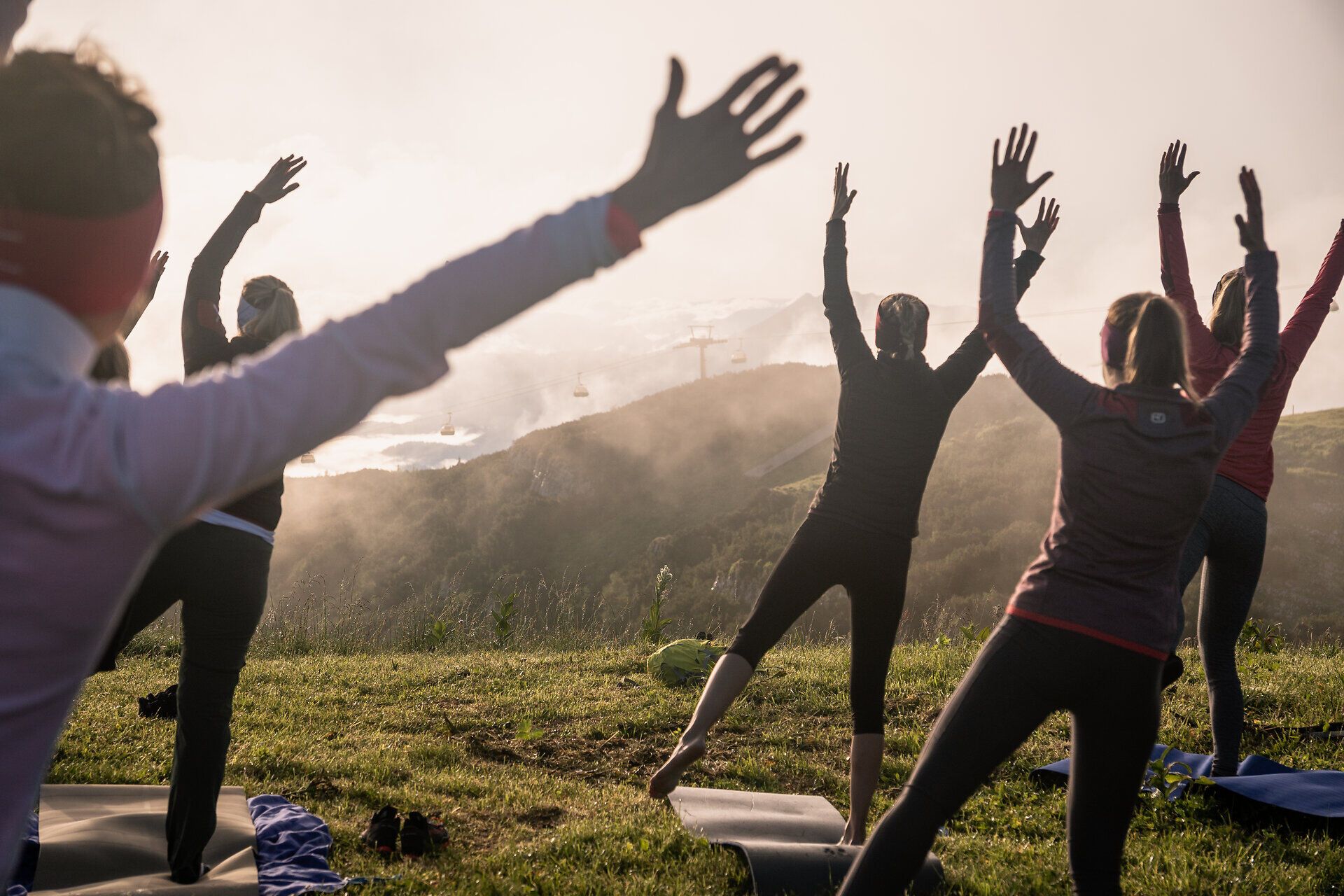 Inmitten der majestätischen Berge findet eine harmonische Yoga-Session statt, während die sanfte Brise die Teilnehmer umhüllt. Die atemberaubende Aussicht auf die umliegenden Täler und Gipfel schafft eine friedliche Atmosphäre, die Körper und Geist belebt.
