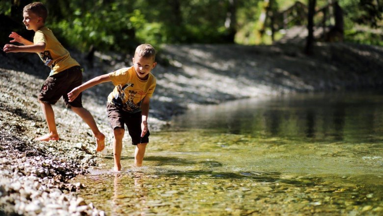 Zwei Kinder spielen am Ufer des klaren Wassers in der Natur.